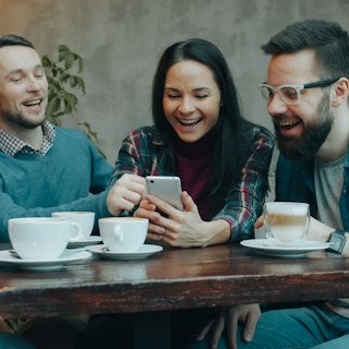 Friends laughing around a phone at a cafe